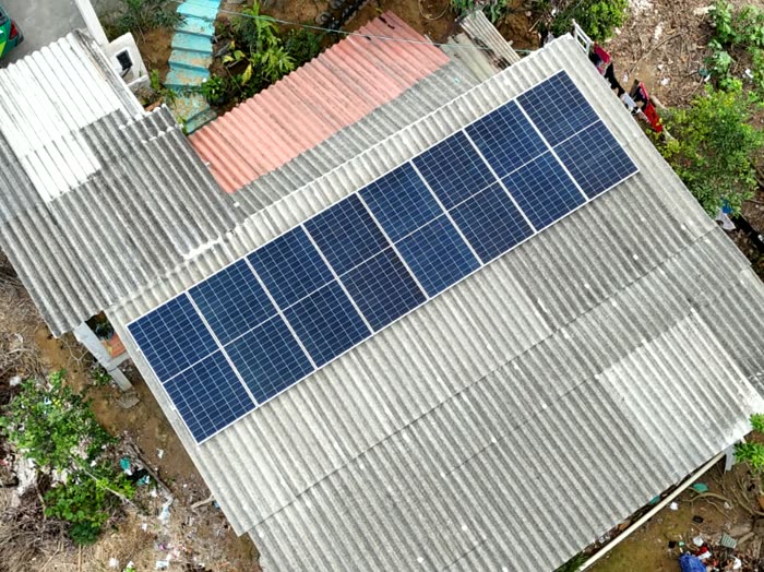 Vista de cima de uma casa com placas solares no telhado, vista da rua e árvores em volta
