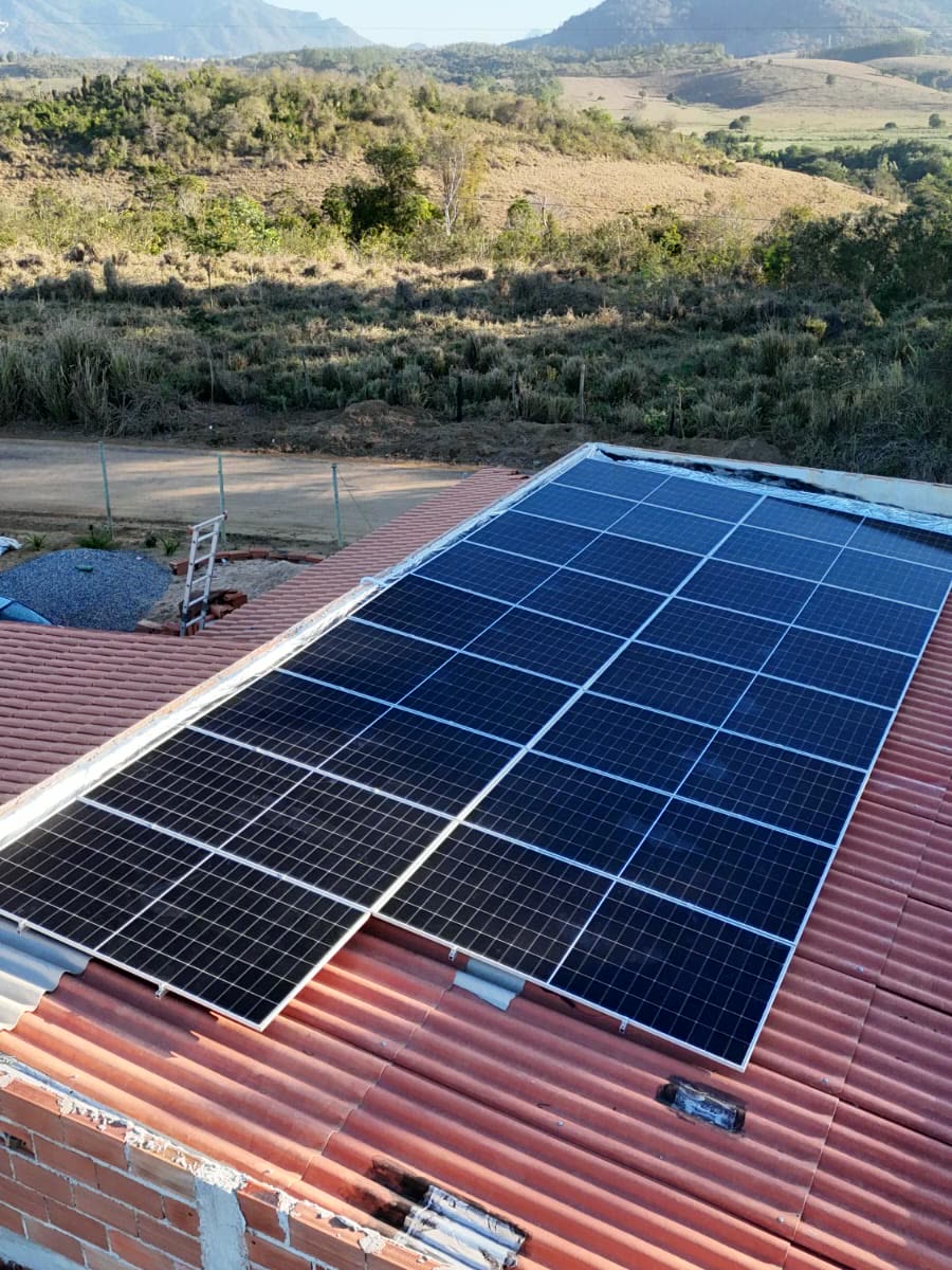 Placas solares instaladas sobre telhado de telha vermelha, com a serra ao fundo